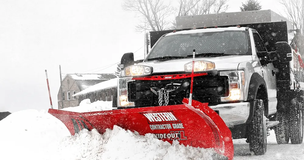 A snow plow is driving down a snowy street.
