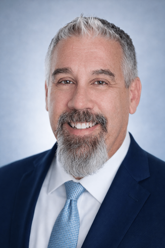Professional headshot of Clifton, a smiling man in a navy suit, light blue shirt, and tie against a soft blue background