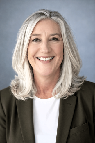 Cyndi, Smiling woman with shoulder-length gray hair in a dark jacket against a gray backdrop