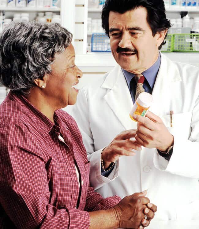 Pharmacist in white coat showing pill bottle to customer at a pharmacy counter