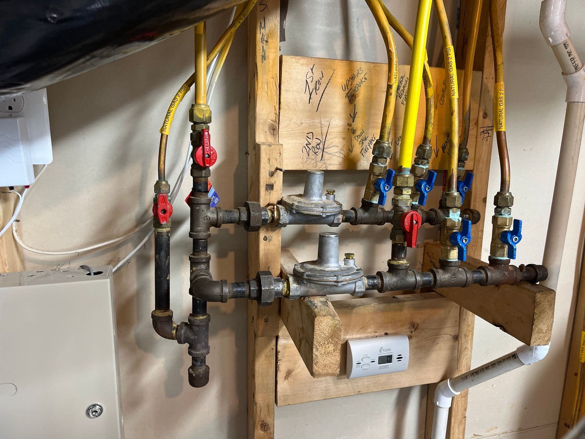 Gas manifold with yellow and copper pipes, valves, and regulators on a wooden frame.