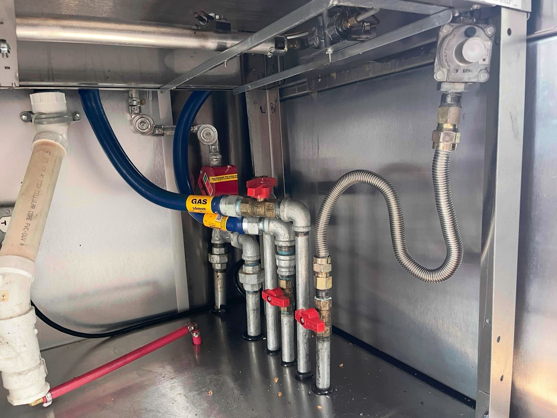 Plumbing system with red and yellow valves, pipes, and metal fixtures mounted inside a stainless steel cabinet.