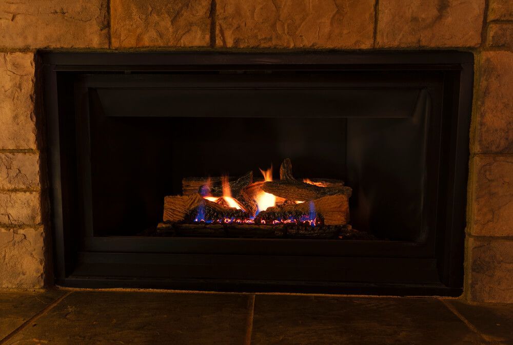 Fireplace with burning logs and flames, set in a dark frame against a stone wall.