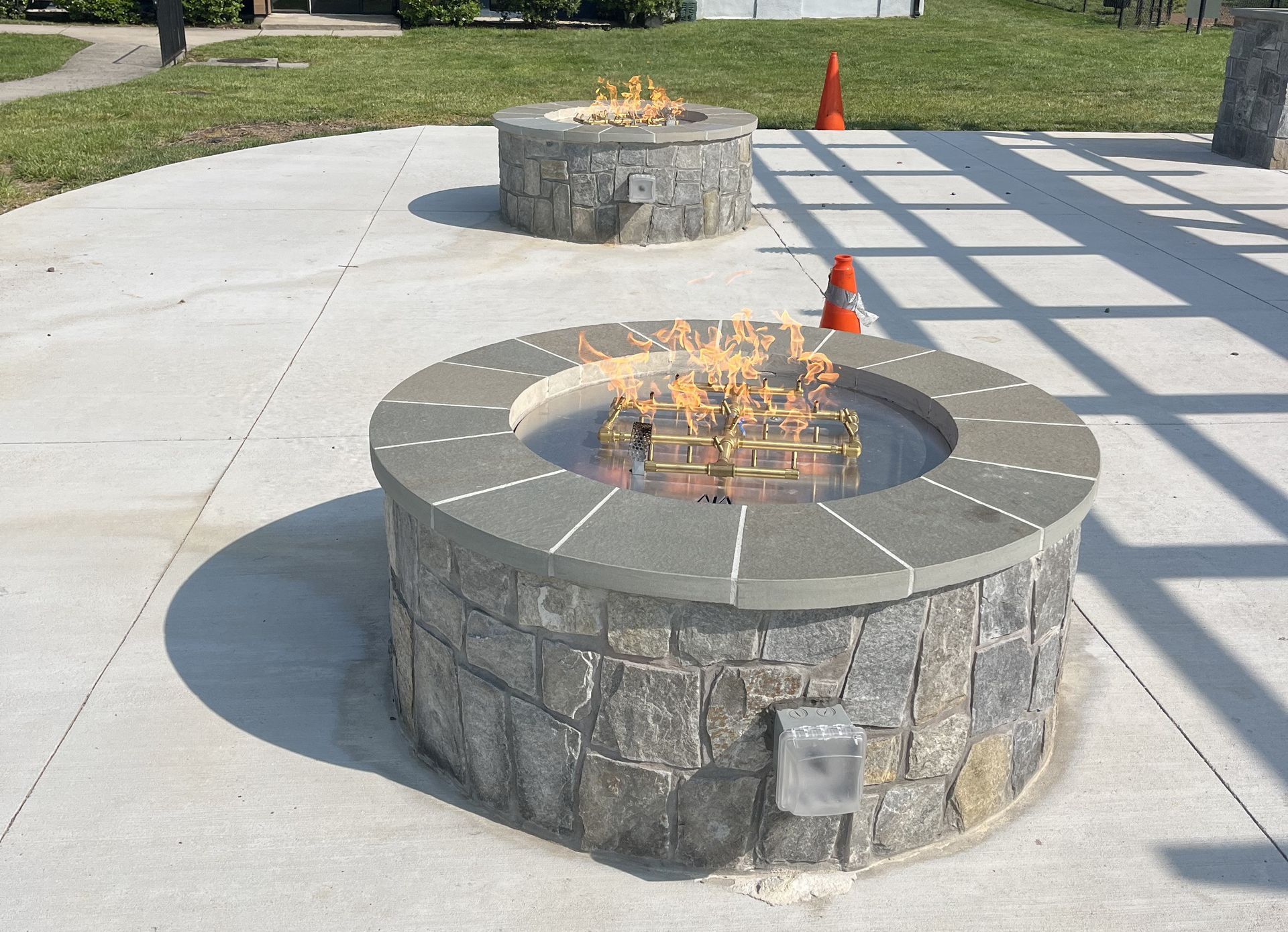 Two Lit Stone Fire Pits On A Concrete Patio Orange Cones In The Background — Falls Church, VA — Nova Gas Two Lit Stone Fire Pits On A Concrete Patio Orange Cones In The Background — Falls Church, VA — Nova Gas