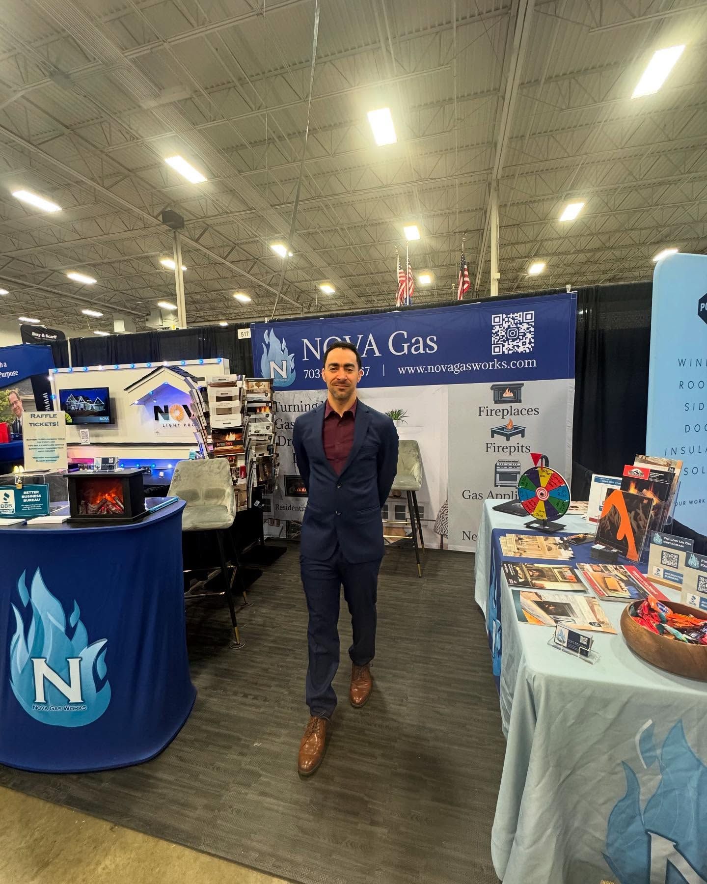 A person in a blue suit stands at a Nova Gas trade show booth with blue branding, a display, and a table of materials.