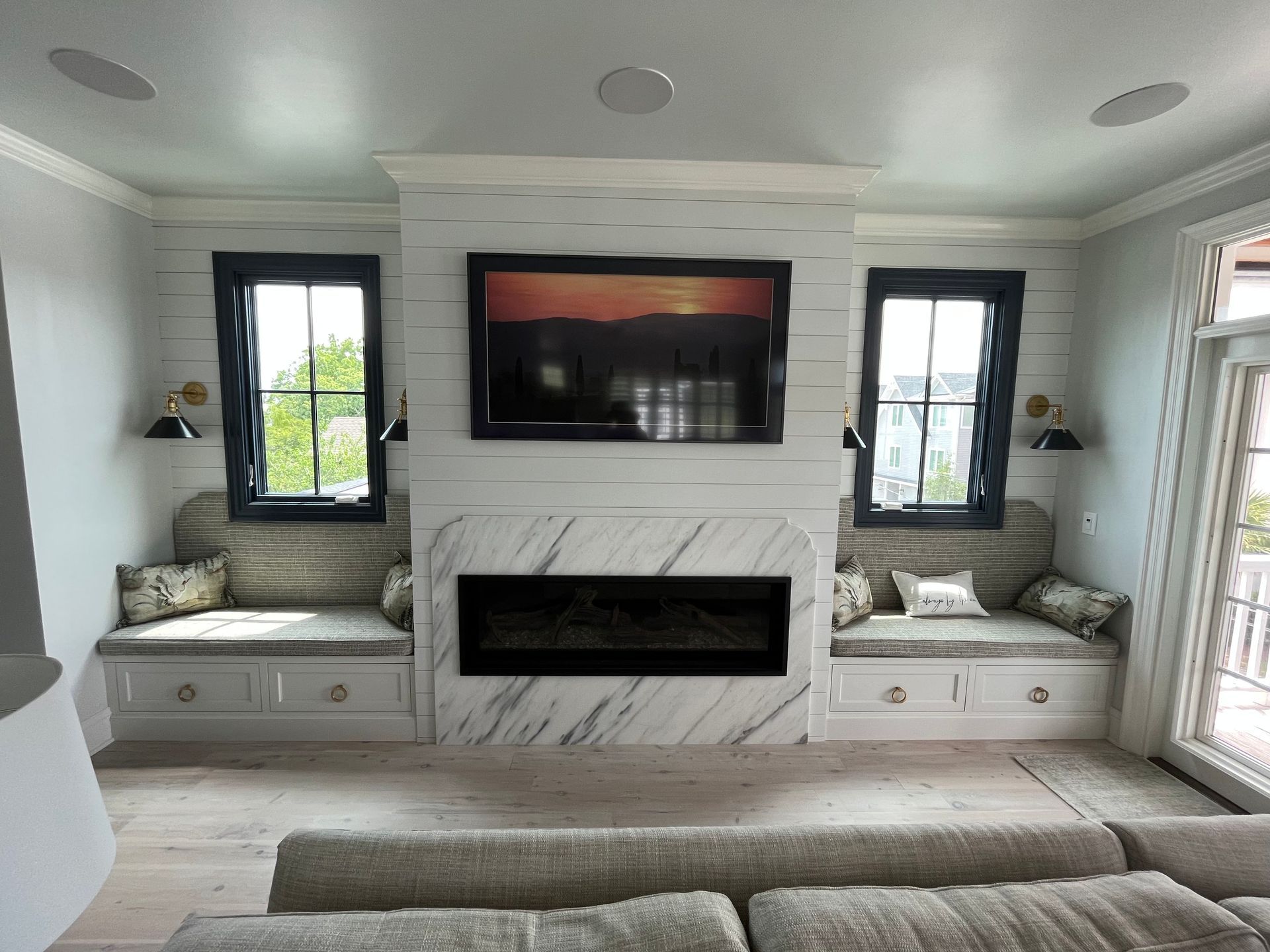 Modern living room with marble fireplace, wall-mounted TV, and twin windows with built-in benches