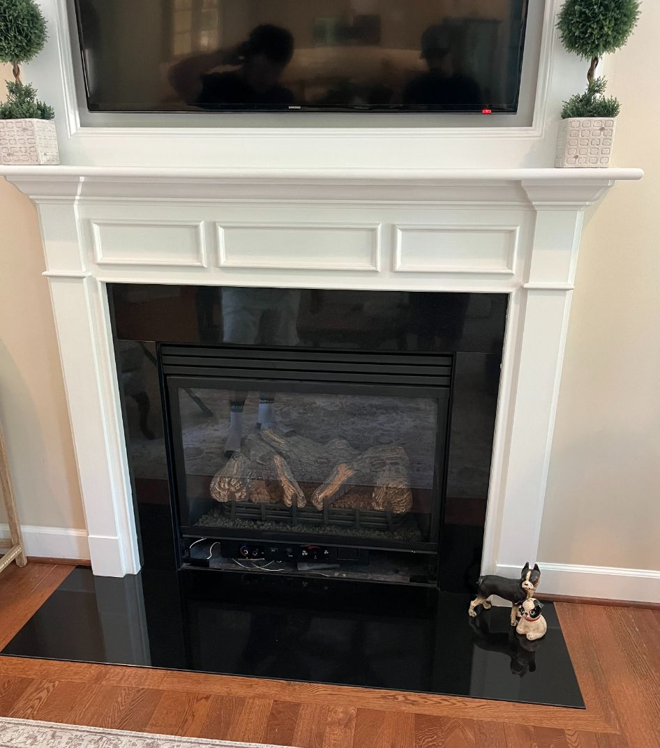 Gas fireplace with black surround and white mantel, TV above, and rug in front.