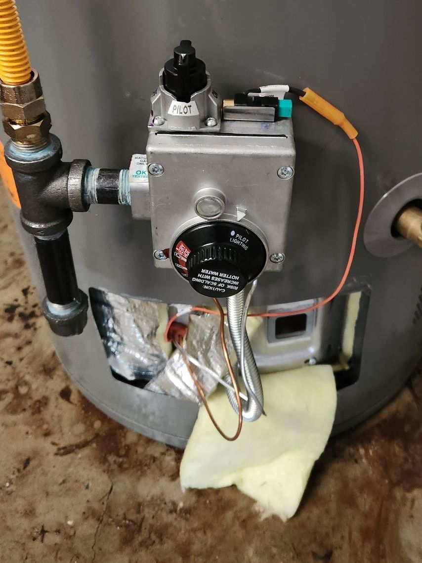 Close-up of a gas water heater's control panel and gas line connection, with insulation and wires visible.