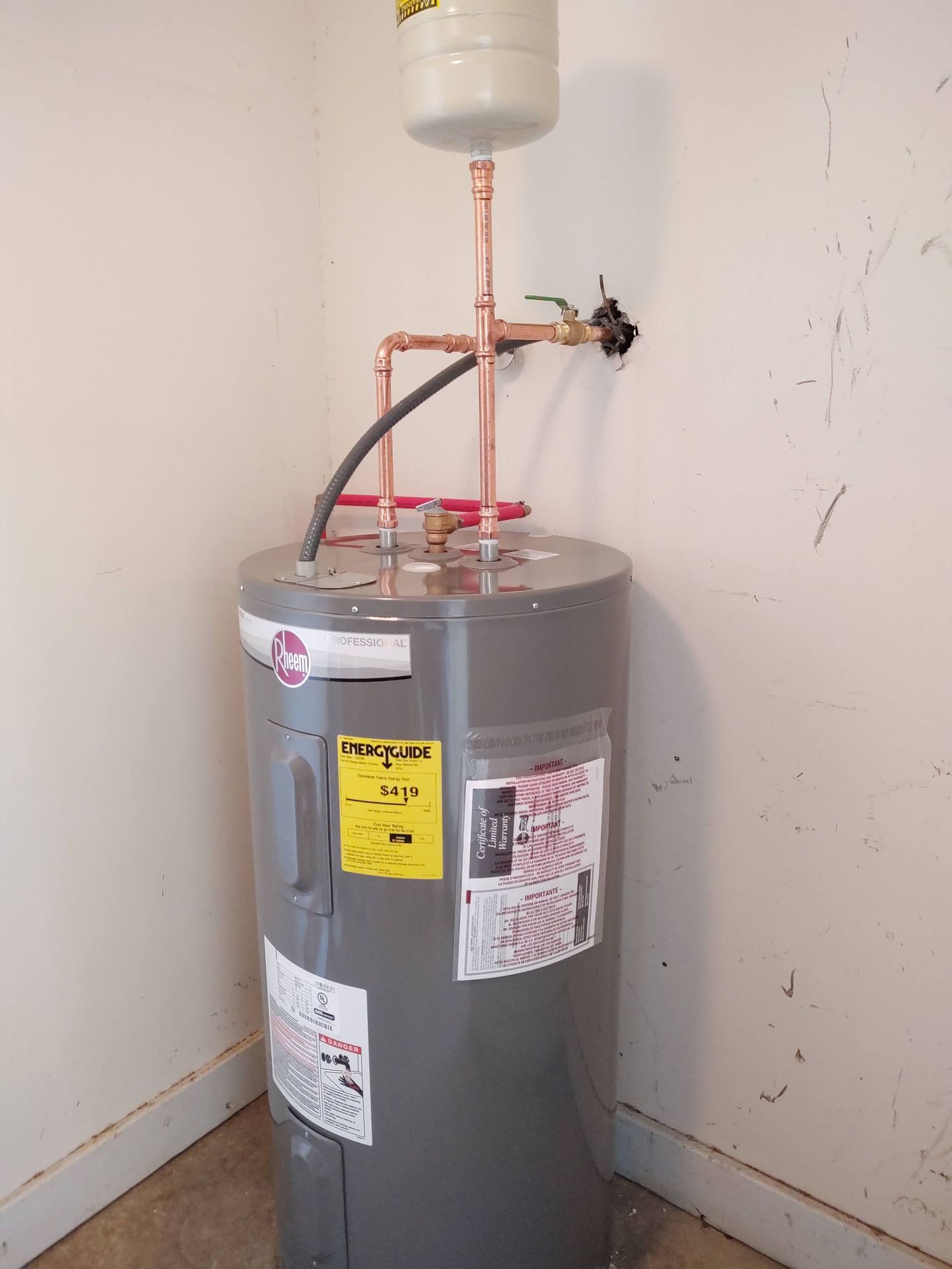 A gray water heater with copper pipes, a pressure tank, and control valves in a corner.