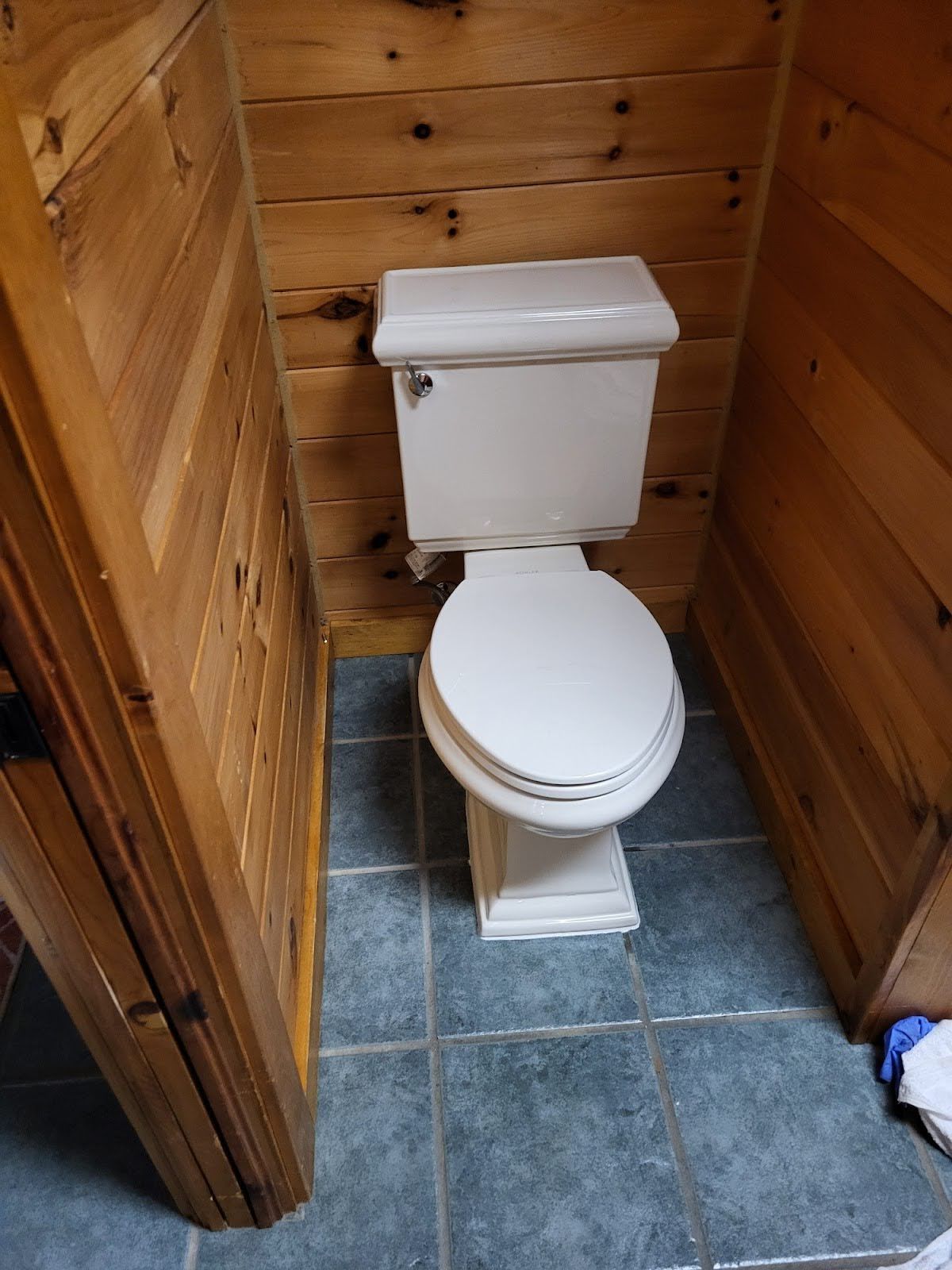 A toilet in a small wooden-paneled room with blue-tiled floor.