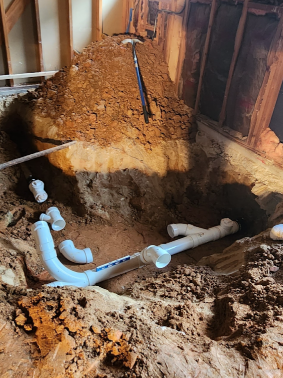 Trench with broken irrigation pipe being repaired with a Y-fitting and clamps; water pooled in the dirt.