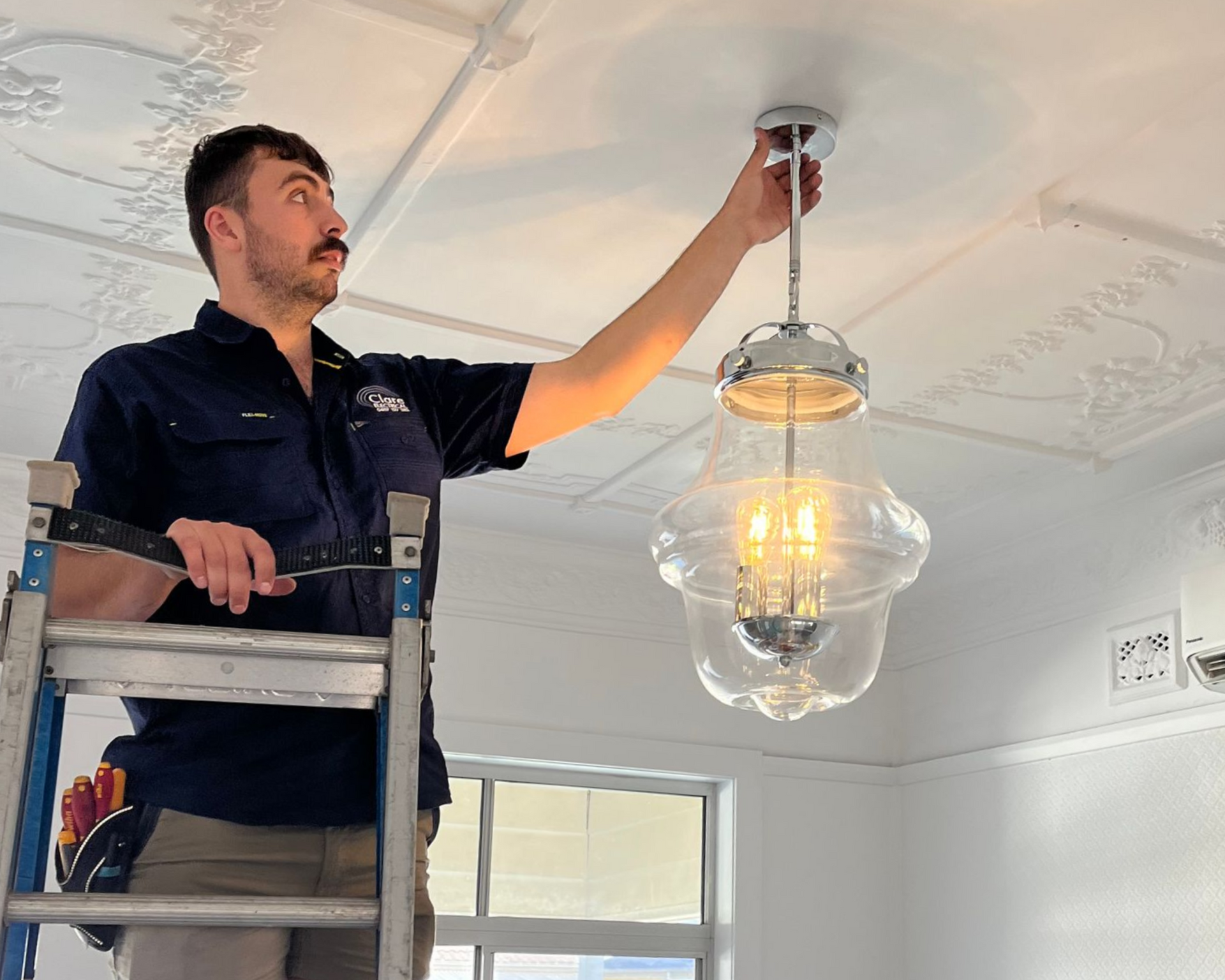 Two People Installing a Water Heater in a Bathroom — Abode Electrical in Tighes Hill, NSW