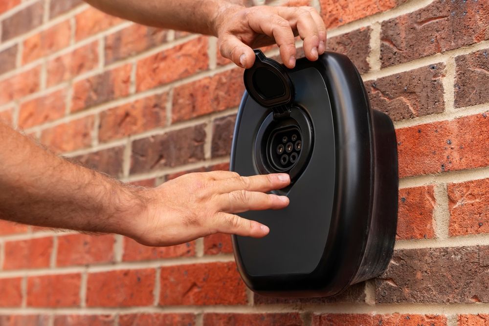 Hands Opening the Charging Port on a Black EV — Abode Electrical in Tighes Hill, NSW