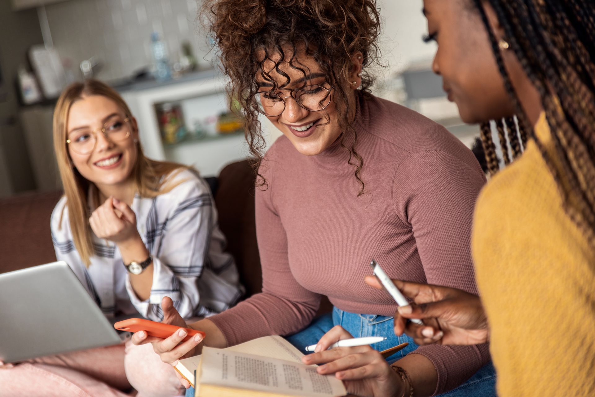 A group of young women are sitting on a couch looking at a tablet.