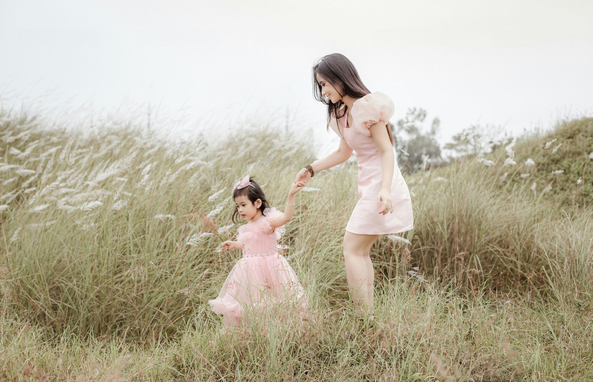 A woman and a little girl are holding hands in a field.