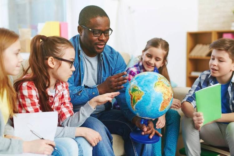 Teacher shows globe to students in classroom, pointing.