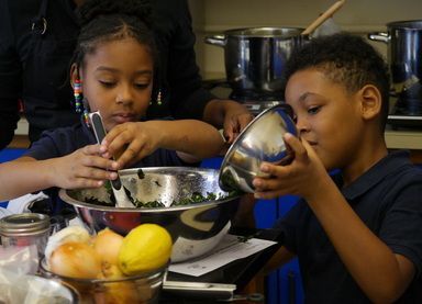 Two children mixing ingredients in a metal bowl in a kitchen.
