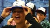 Person wearing a white and blue hat, smiling. Two others in background, wearing similar hats.