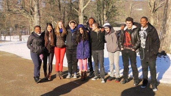 Group of diverse teens standing on path with snow, sunny day.