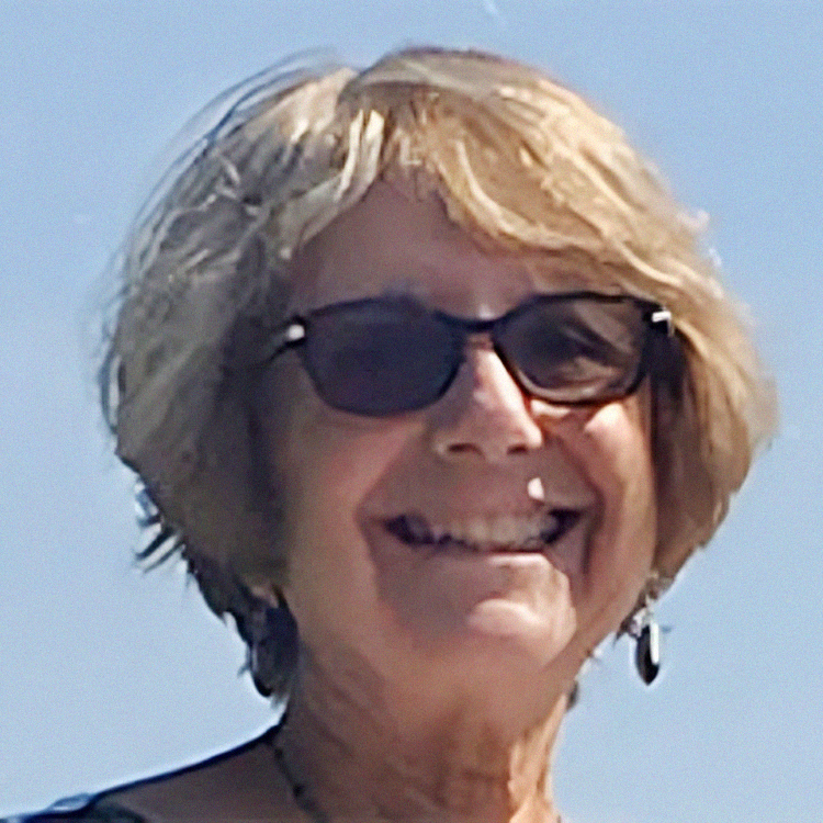 Woman with blonde hair and sunglasses smiling outdoors.