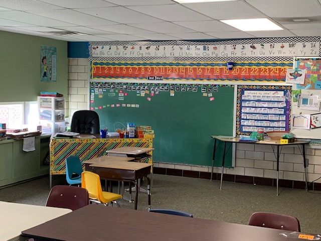 Empty classroom with green chalkboard, teacher's desk, and student desks.