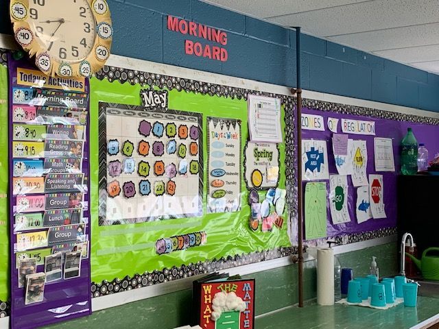 Classroom morning board with clock, calendar, and student work; green and purple accents.