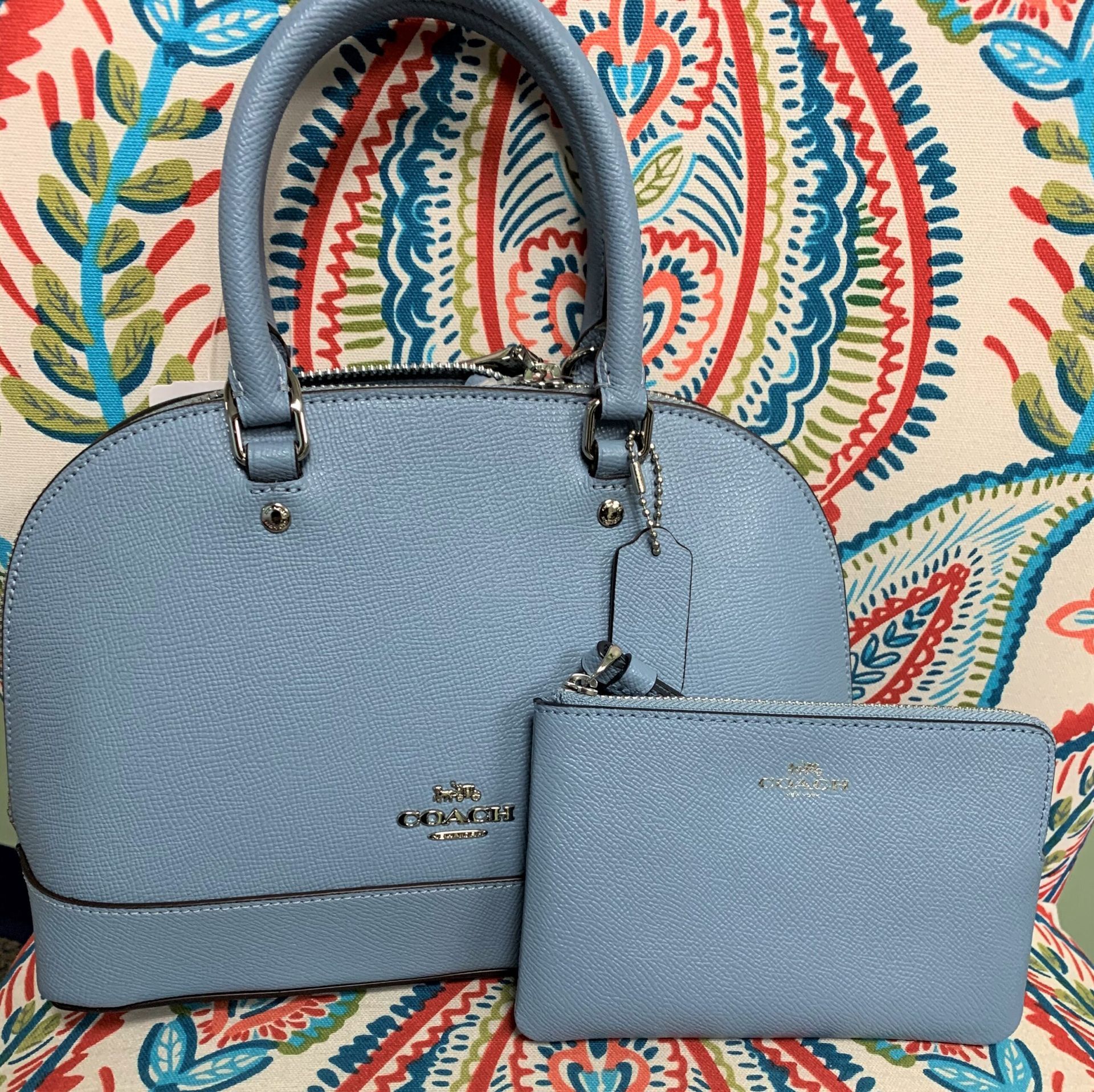 Light blue Coach handbag and matching pouch on patterned fabric.