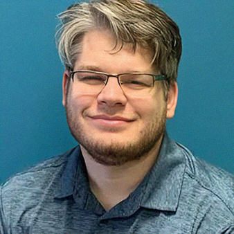 Man with glasses, graying hair, and beard smiles at the camera against a teal background.