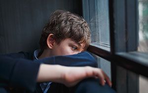 A young person, arms crossed, sadly gazing out a window.
