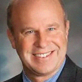 Smiling older man in a blue shirt and black blazer.