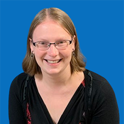 Woman with glasses smiles at the camera against a blue background, wearing a black top.