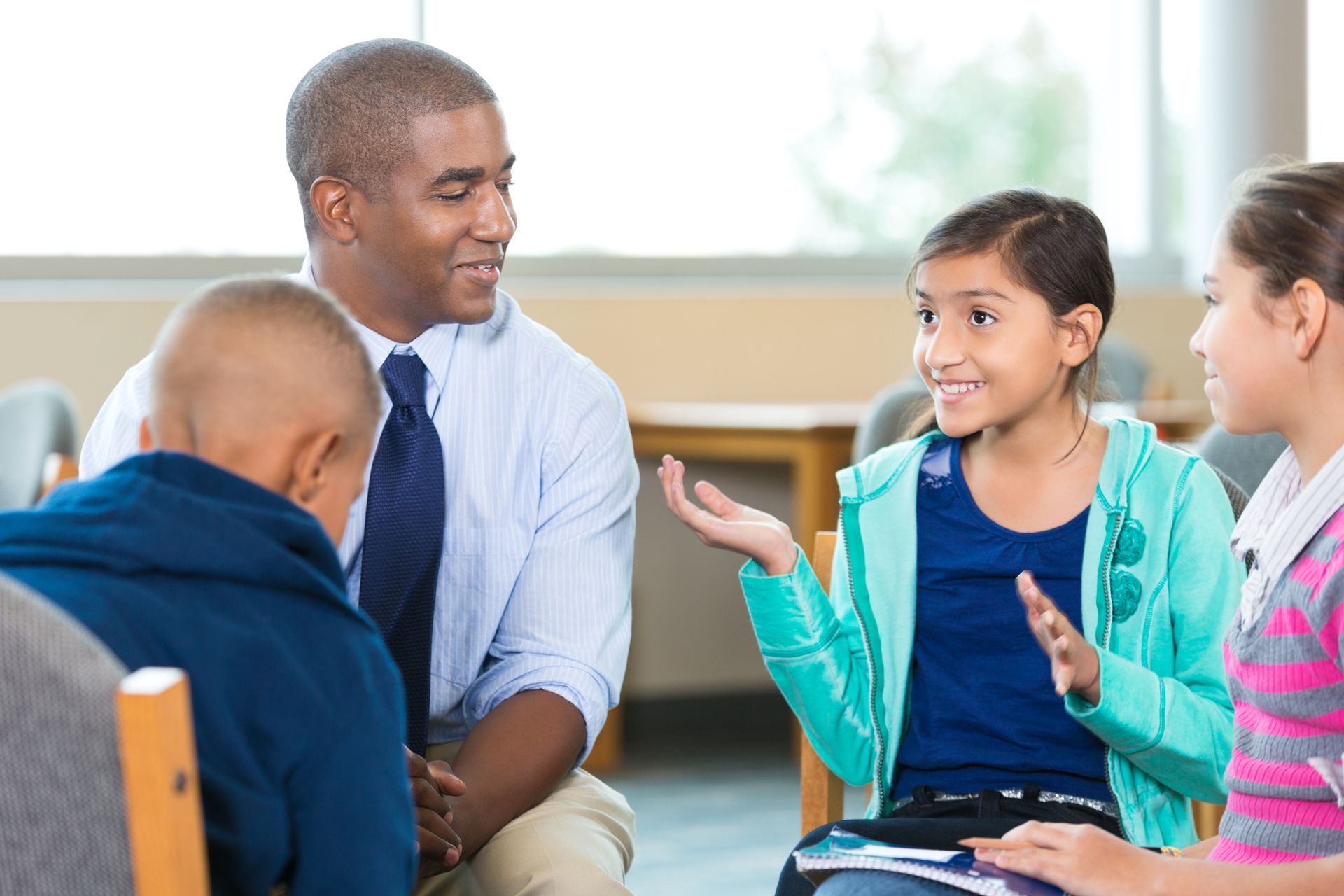 Group therapy session: Man smiles at girl gesturing while two other children listen.