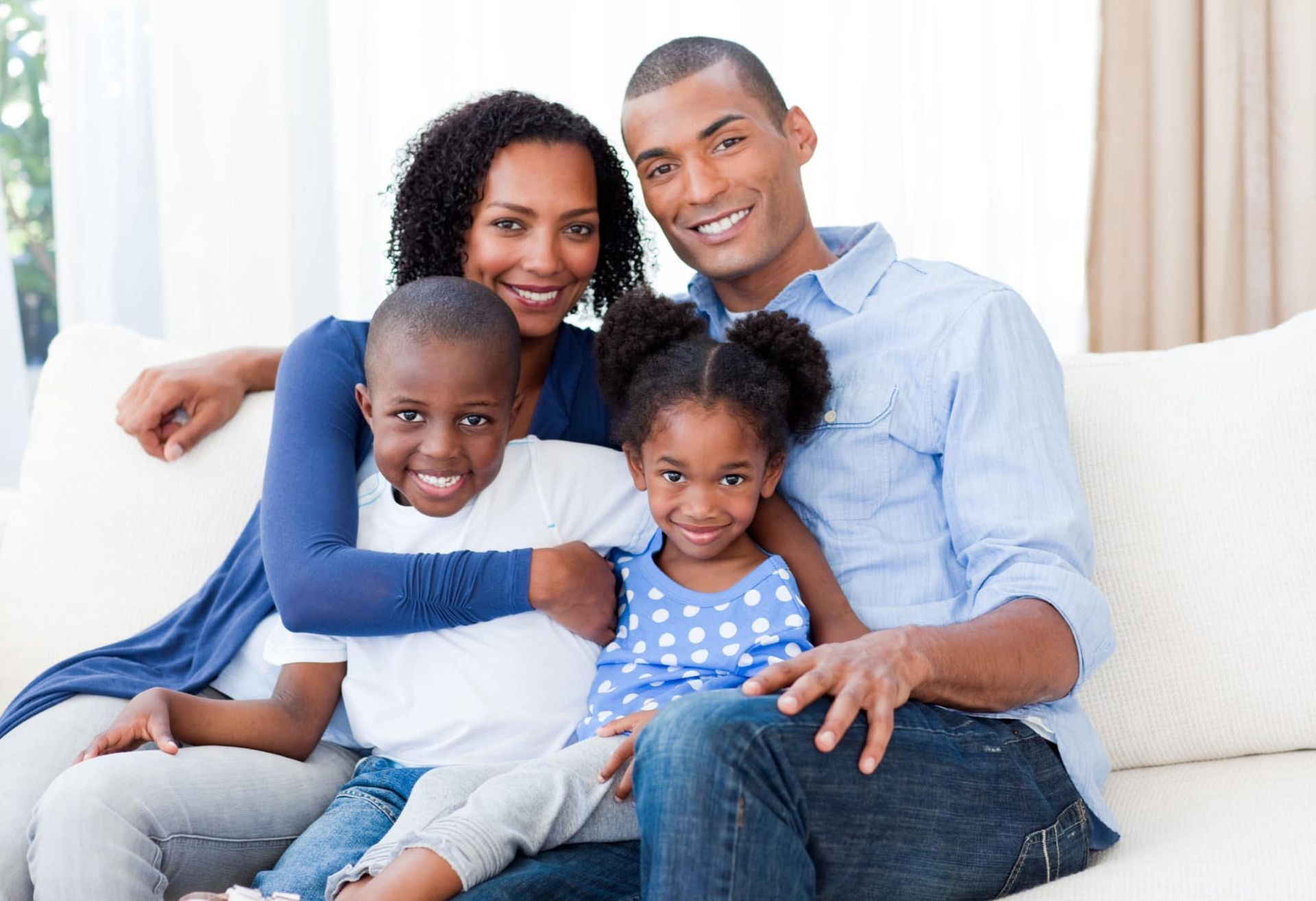 Family of four smiling on a couch; parents hugging children.
