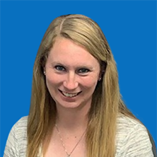 Blonde woman smiles at camera, wearing a light sweater, blue background.