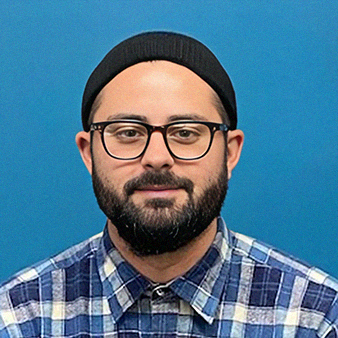 Man with glasses, beard, and black beanie, wearing a plaid shirt, smiling at the camera.