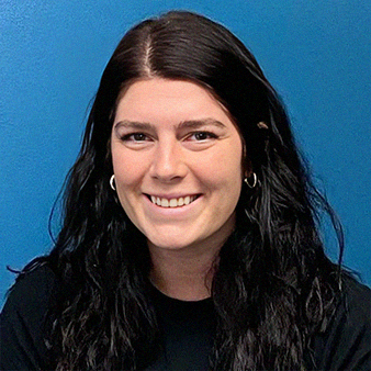 Woman with dark hair smiling in front of a blue wall.