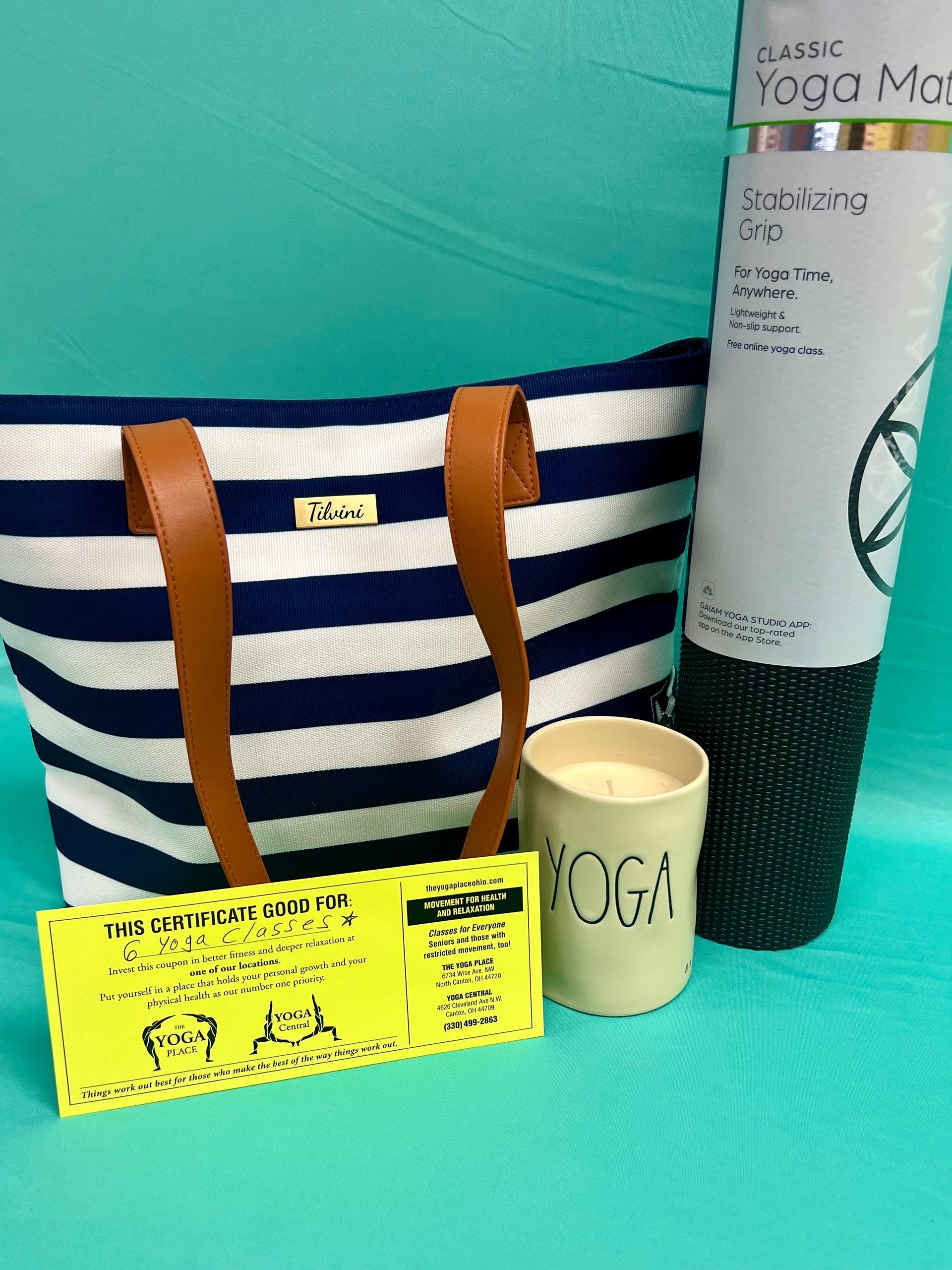 A yoga gift set: striped tote, mat, candle, ticket, on teal background.
