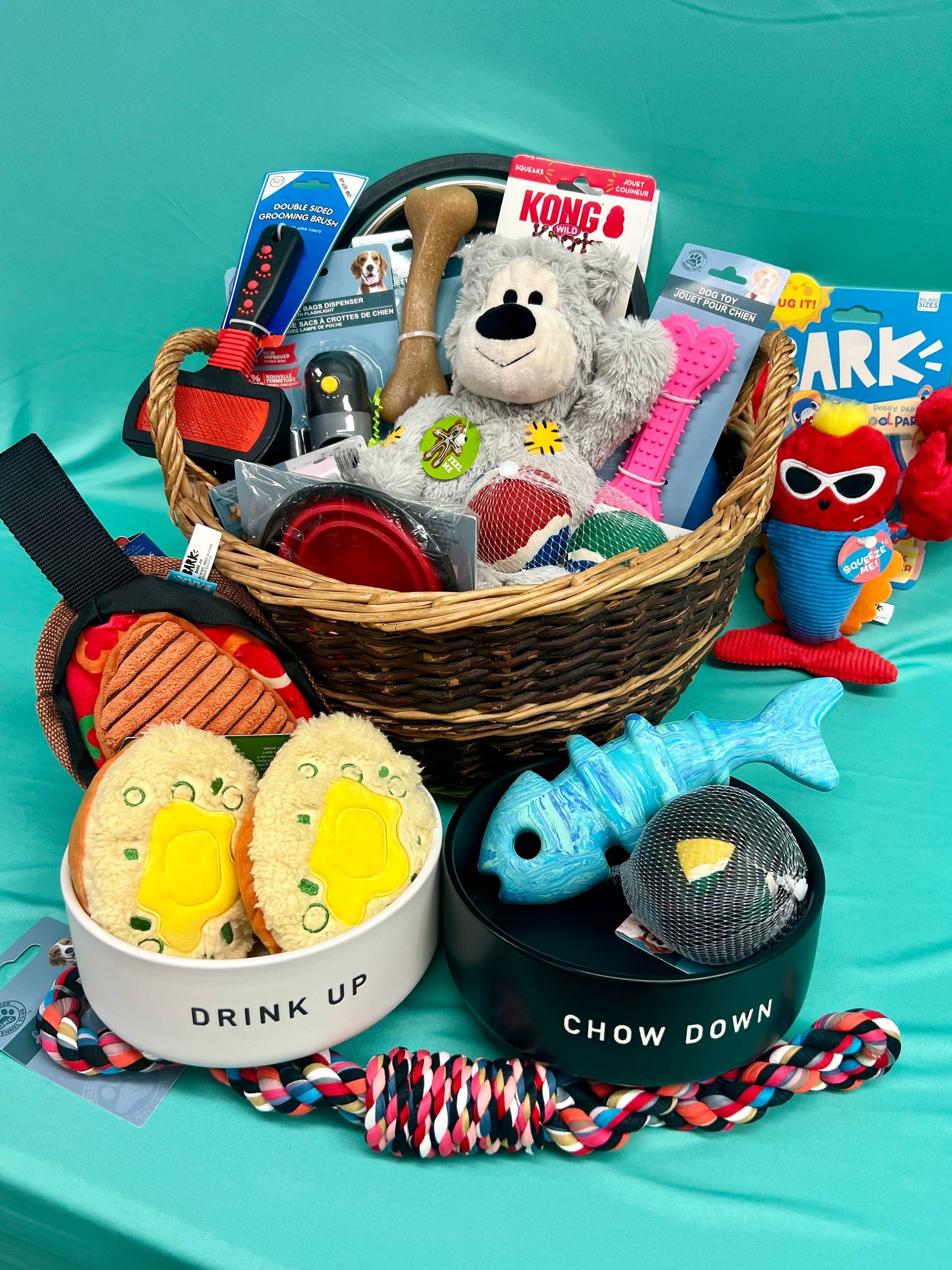 Dog toy gift basket with food bowls and rope on a teal surface.