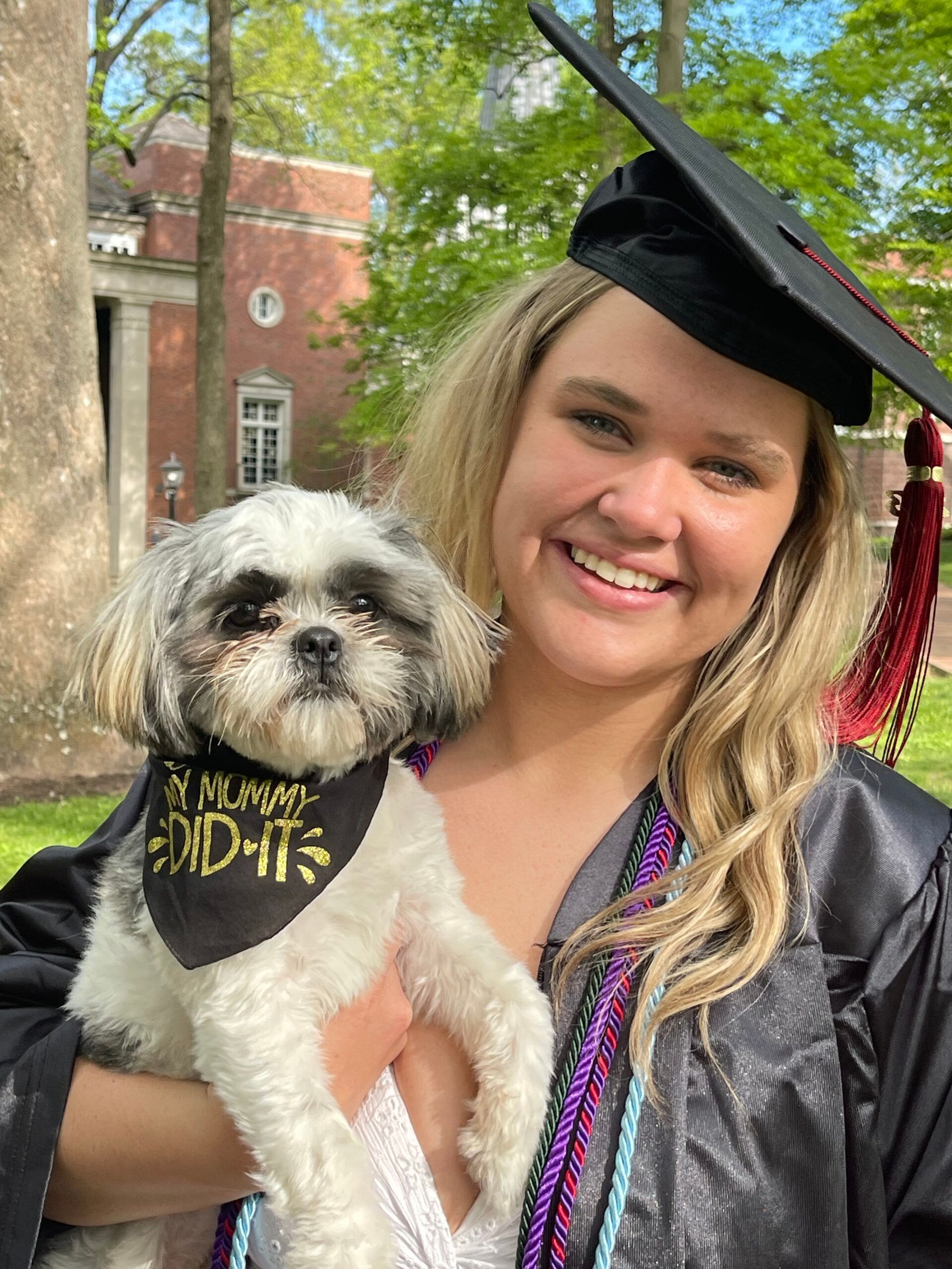 Woman in graduation gown holding a dog wearing a