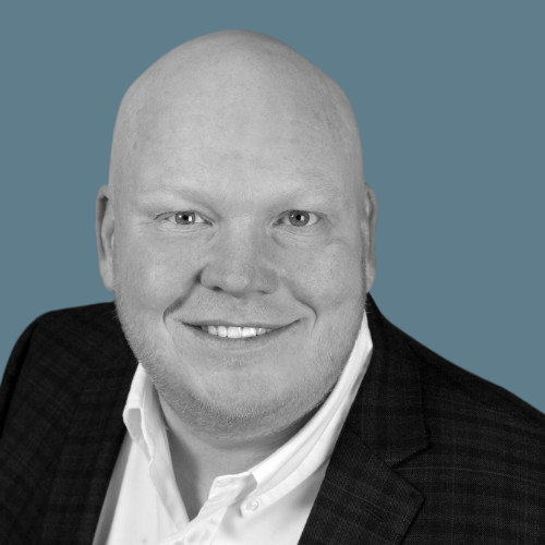 Bald man in a blazer smiling, headshot against a blue background.