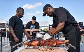 Three men preparing a roasted pig outdoors. One carves the meat, the others watch.