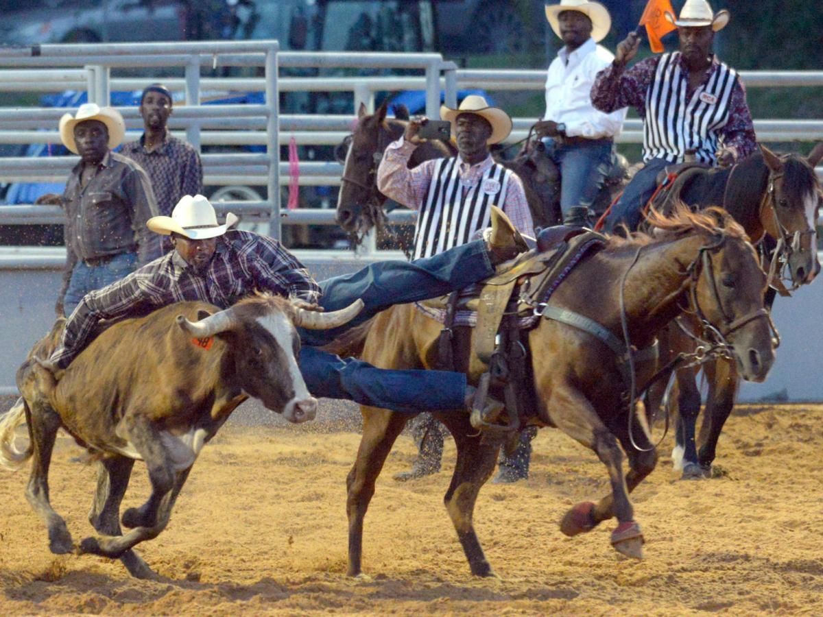 Cowboy attempting to wrestle a steer in a rodeo, with other riders and spectators in the background.