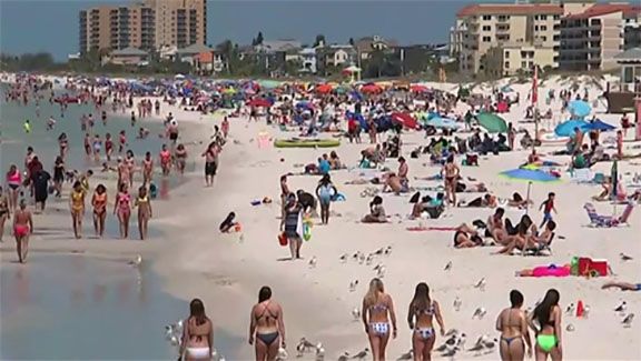 People at a crowded beach with buildings in the background on a sunny day.