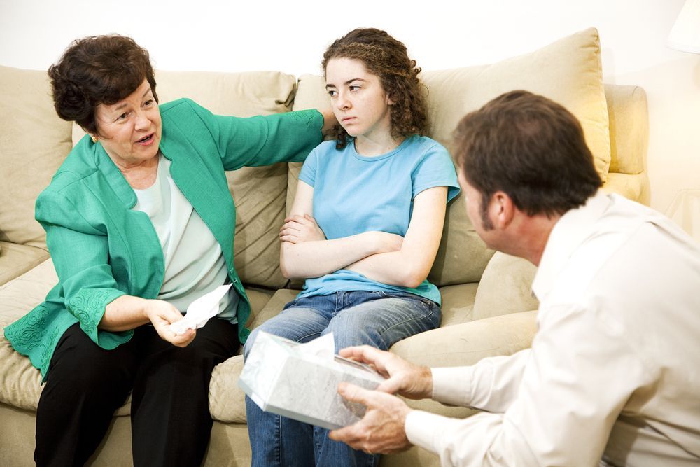 A concerned family: a woman in green comforts a teen girl; a man offers tissues.