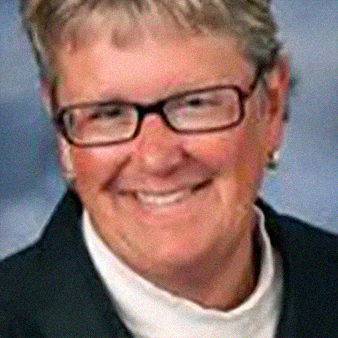 Woman with glasses smiles, wearing a black blazer and white shirt, set against a blurred background.