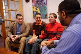 Four people in a room, three on a sofa, one in the foreground; all are smiling, and one person is in a blue shirt.