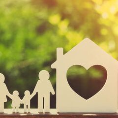 Silhouette of family and house with heart cutout against a blurred green and yellow background.
