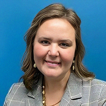 Woman with brown hair, wearing a gray blazer and gold jewelry, smiles in front of a blue background.