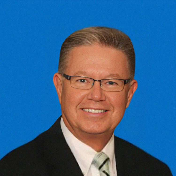 Man with glasses smiling, wearing a suit and tie, against a blue background.