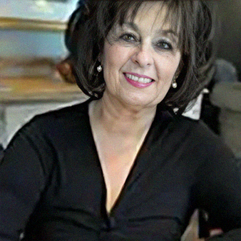 Woman with dark hair smiles, wearing a black top and pearl earrings.